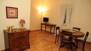 Un comedor con una mesa redonda, sillas, un armario de madera, una lámpara, un televisor y un cuadro enmarcado en la pared.