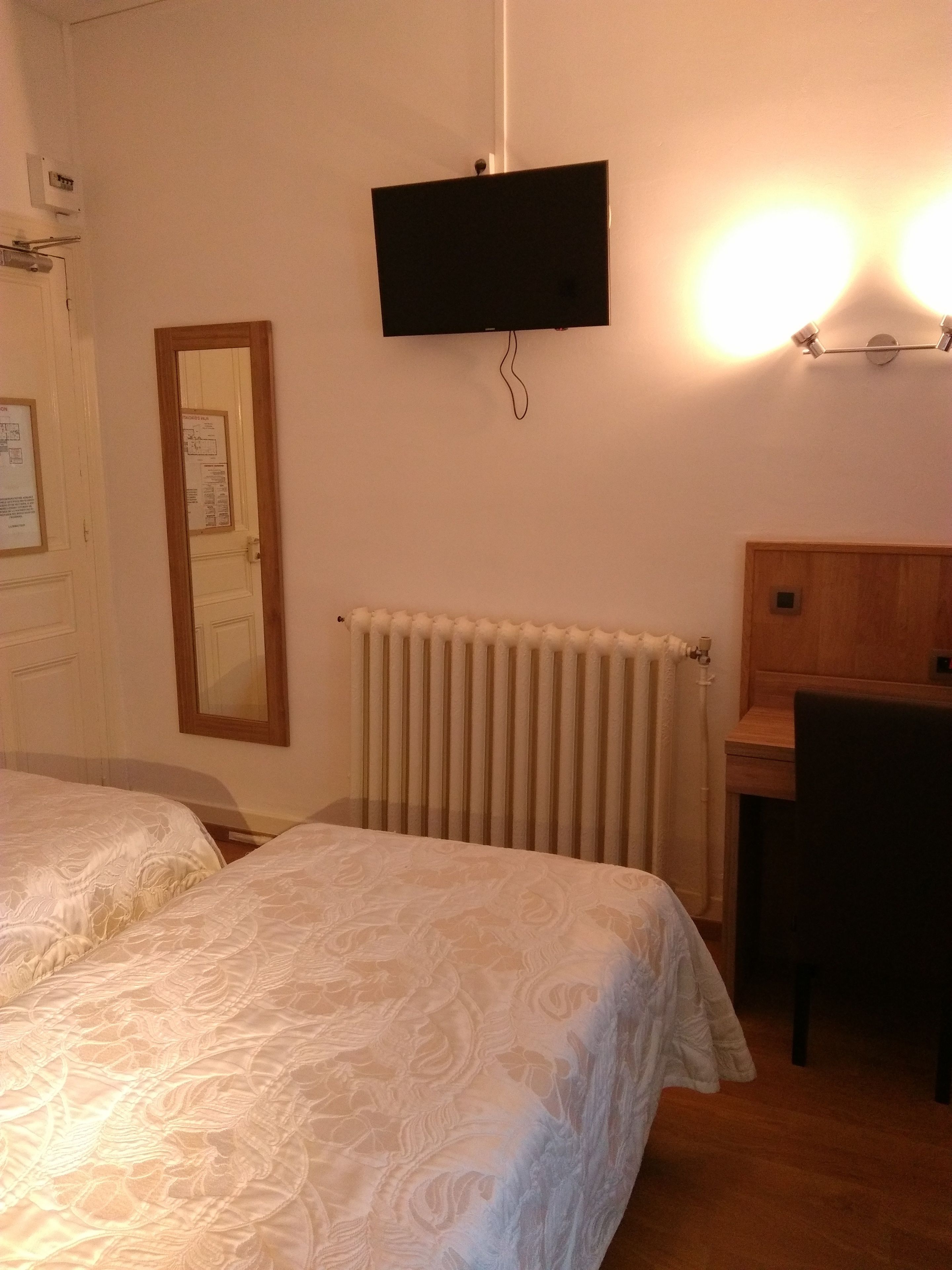 Hotelkamer met twee bedden, een bureau, een stoel, een radiator, een aan de muur bevestigde televisie en een deur met spiegel.
