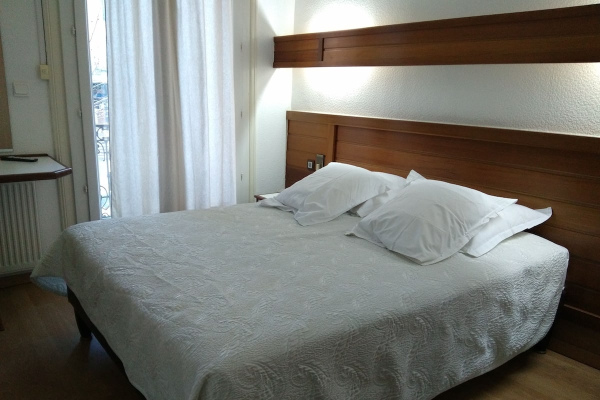 Una cama bien hecha con cabecera de madera, ropa de cama blanca y una ventana con cortinas.