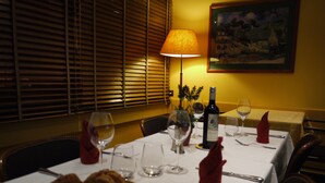 Mesa de jantar posta para dois, com copos de vinho, uma garrafa de vinho e uma cesta de pão.