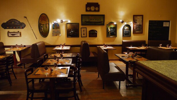 Interior de restaurante com cabines e mesas, piso de madeira e decoração nas paredes, incluindo relógios e quadros.