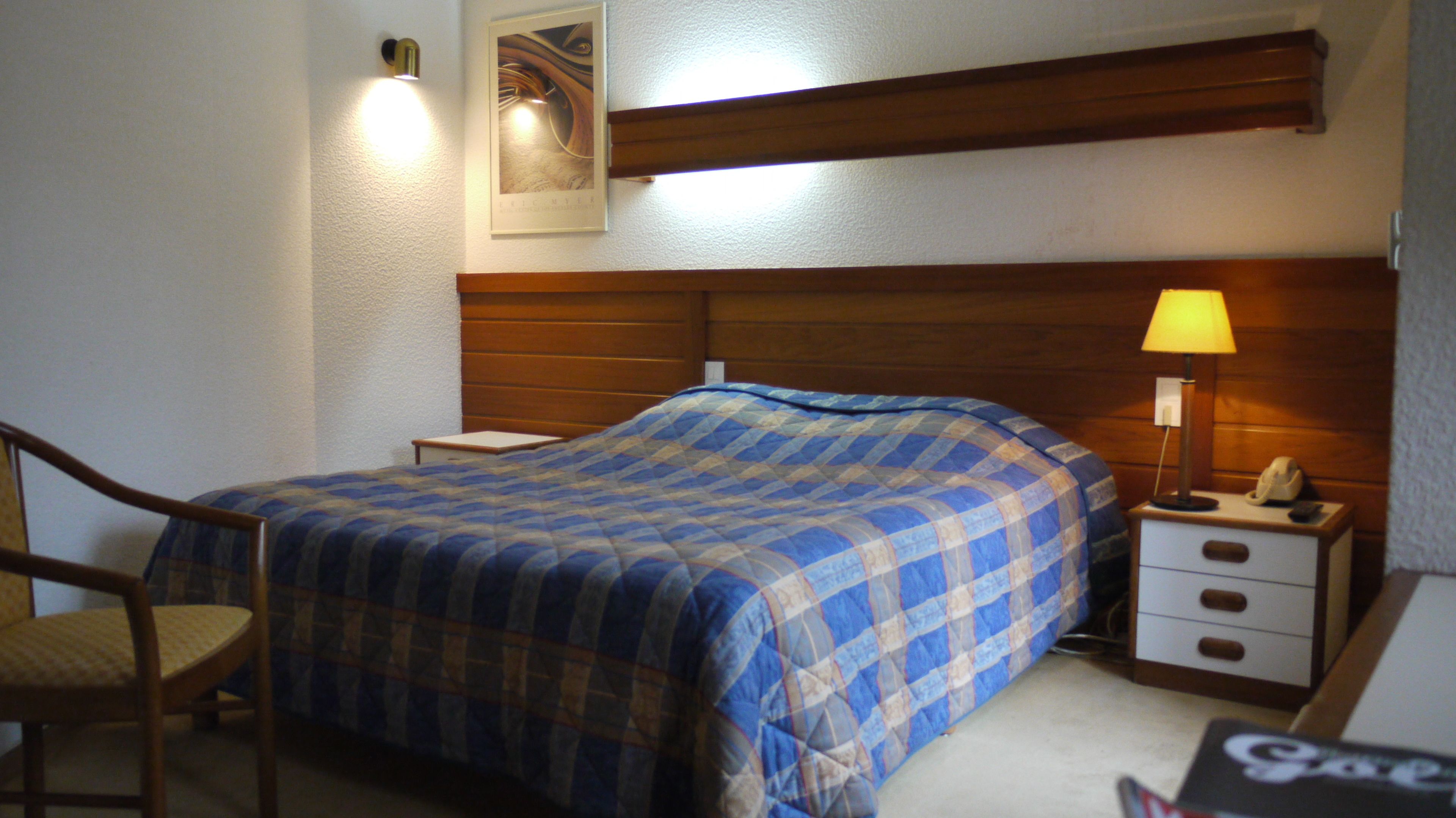 A bedroom with a bed, a nightstand, a chair, and a wall-mounted lamp.