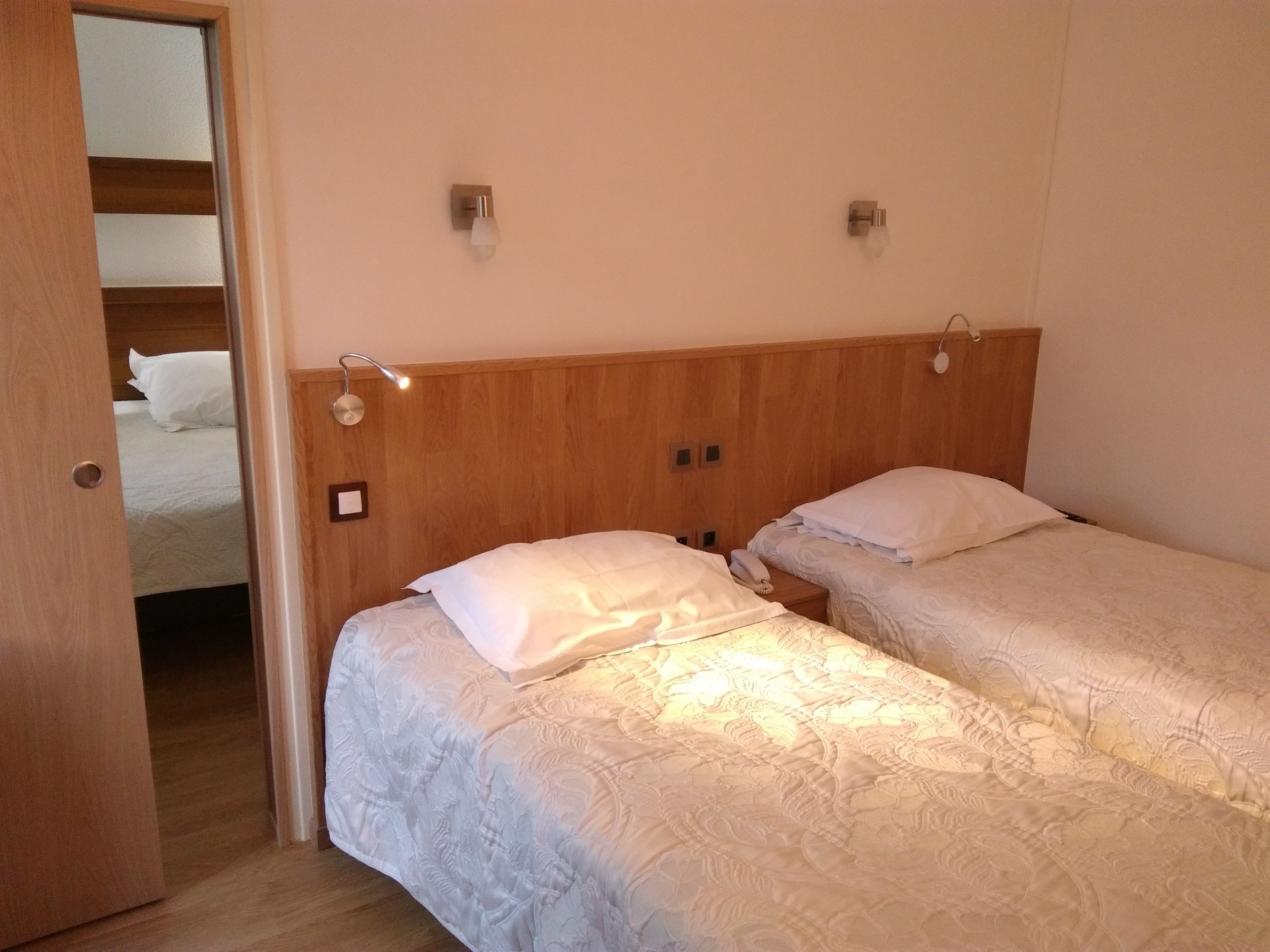 Habitación de hotel con dos camas individuales, cabeceros de madera, lámparas de noche y un armario de madera.