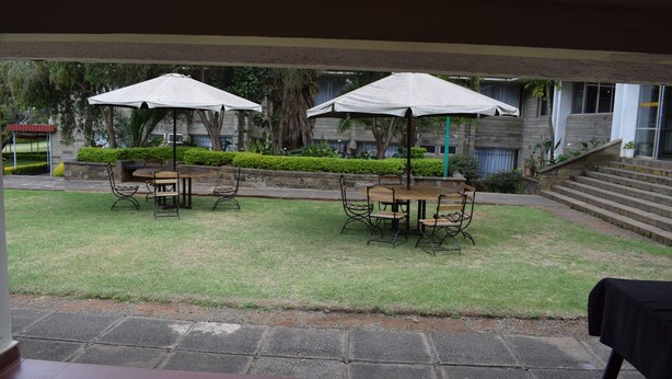 An outdoor patio with tables and chairs under umbrellas, a stone staircase, and a view of a building with a stone facade. - ARC Egerton Hotel (Njoro)