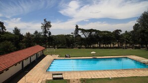 A swimming pool with a tiled deck, surrounded by a grassy area and trees. - ARC Egerton Hotel (Njoro)