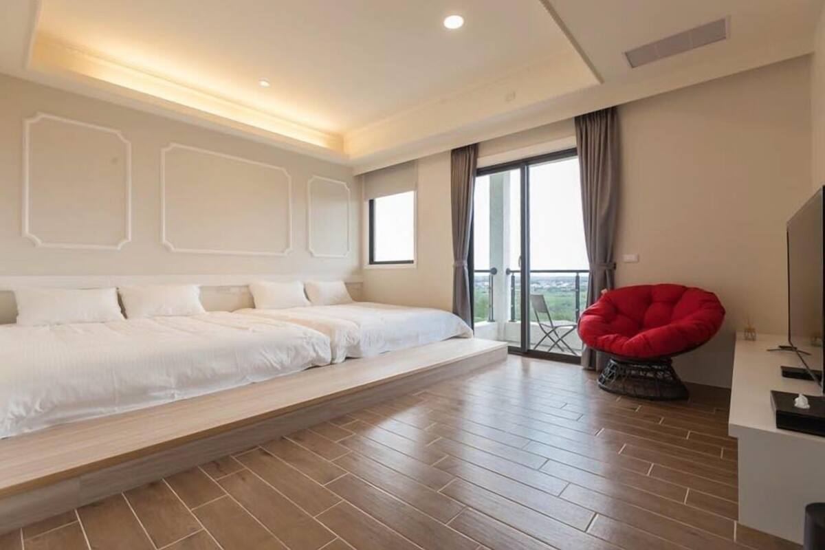 Une chambre moderne avec un grand lit, un fauteuil rouge et un balcon avec vue.