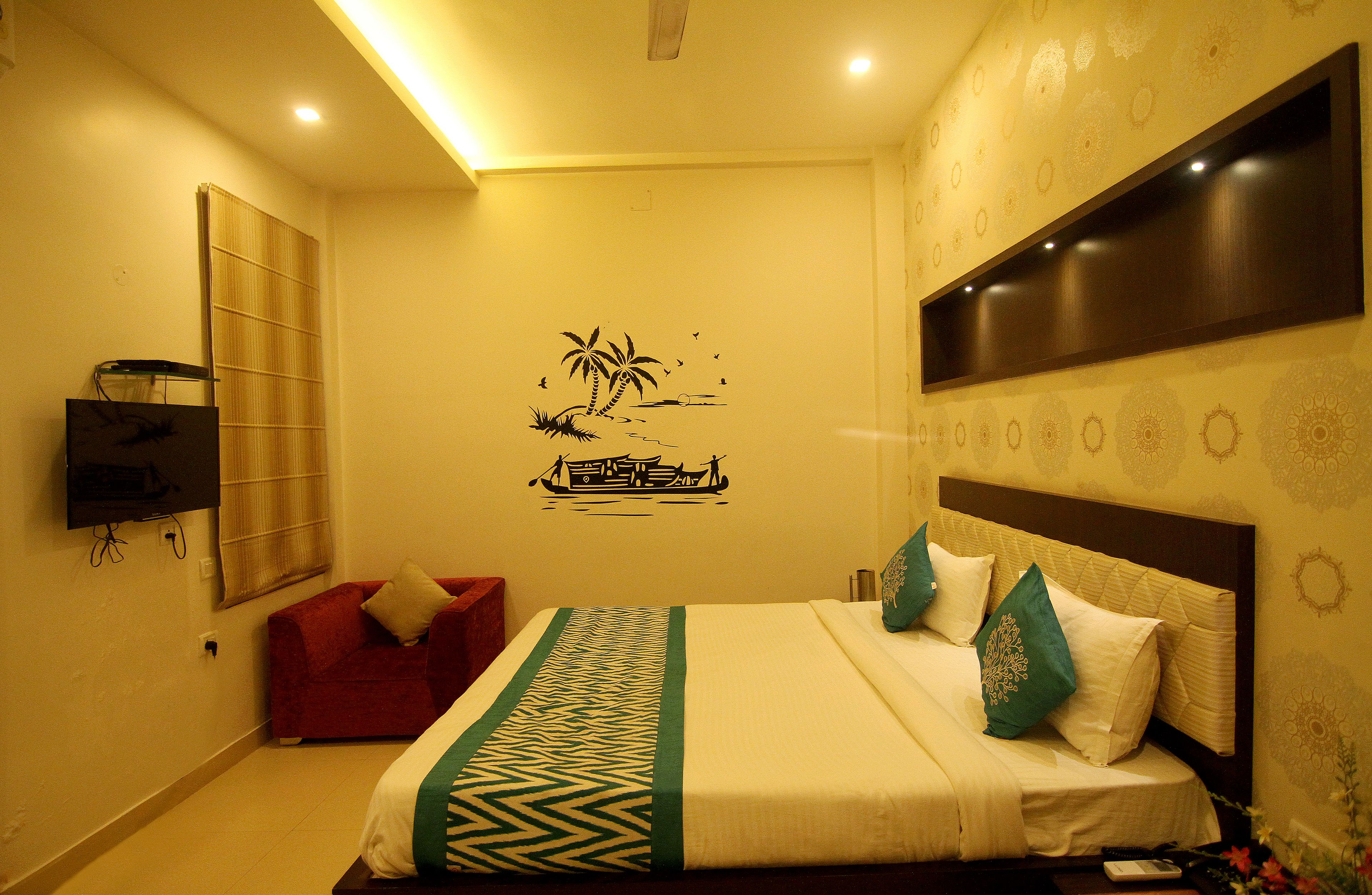 A hotel room with a bed, a red sofa, a wall-mounted TV, and a decorative wall mural.