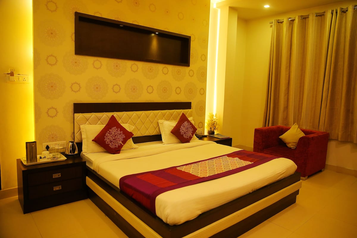 A neatly made bed with a headboard, a bedside table with a lamp, and a red armchair.