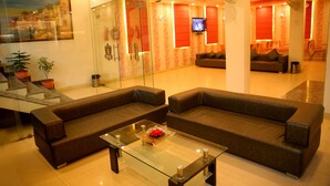 A modern living room with two sofas, a glass coffee table, and a television. - Hotel Rivera Palace (Varanasi)