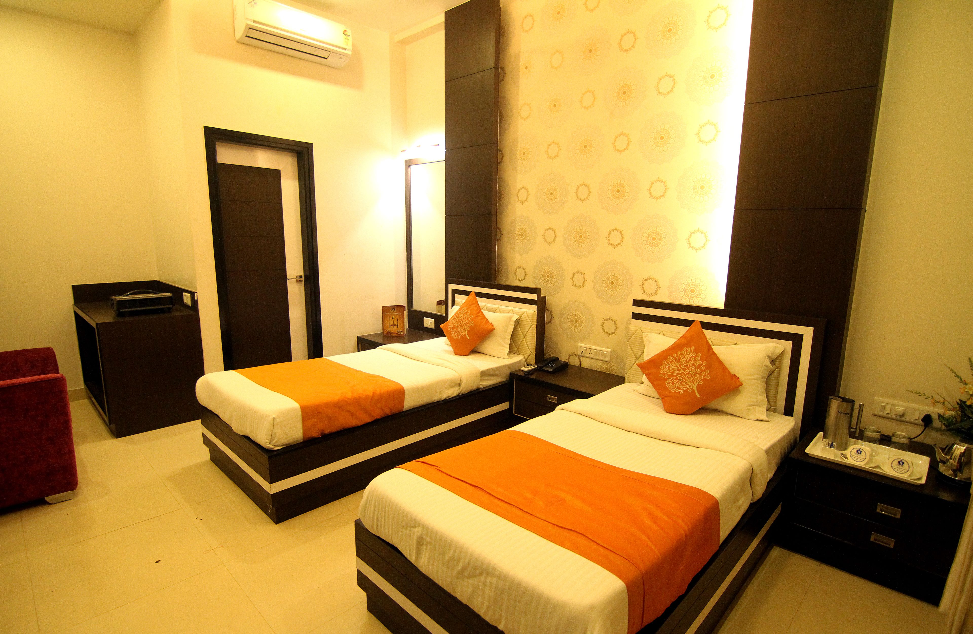 Quarto de hotel com duas camas, uma escrivaninha, uma cadeira e um banquinho vermelho.