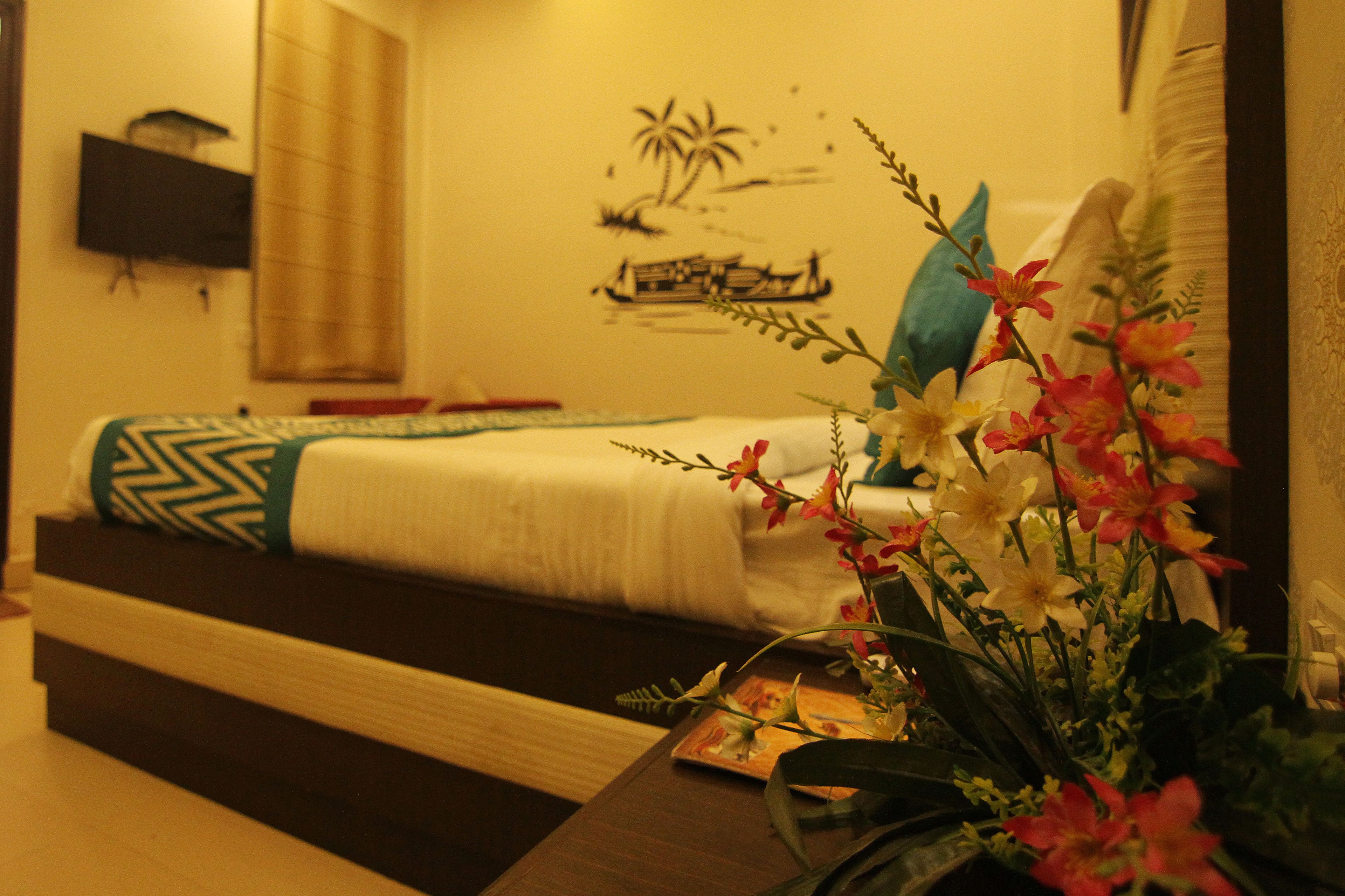 Una camera d'albergo con un letto, un comodino con un vaso di fiori, un affresco e una finestra con persiane.