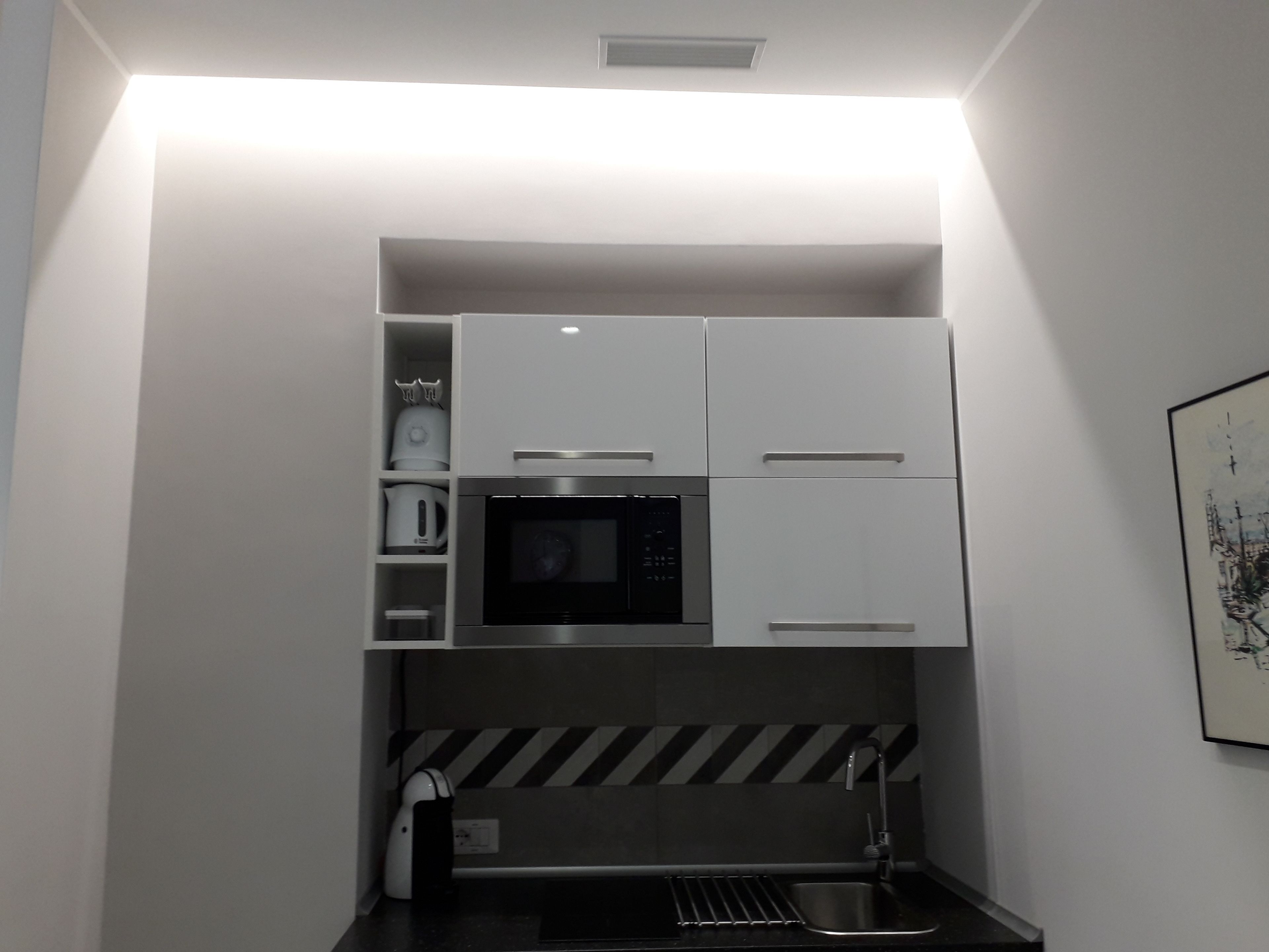 A compact kitchen with white cabinets, a microwave, a kettle, and a sink.