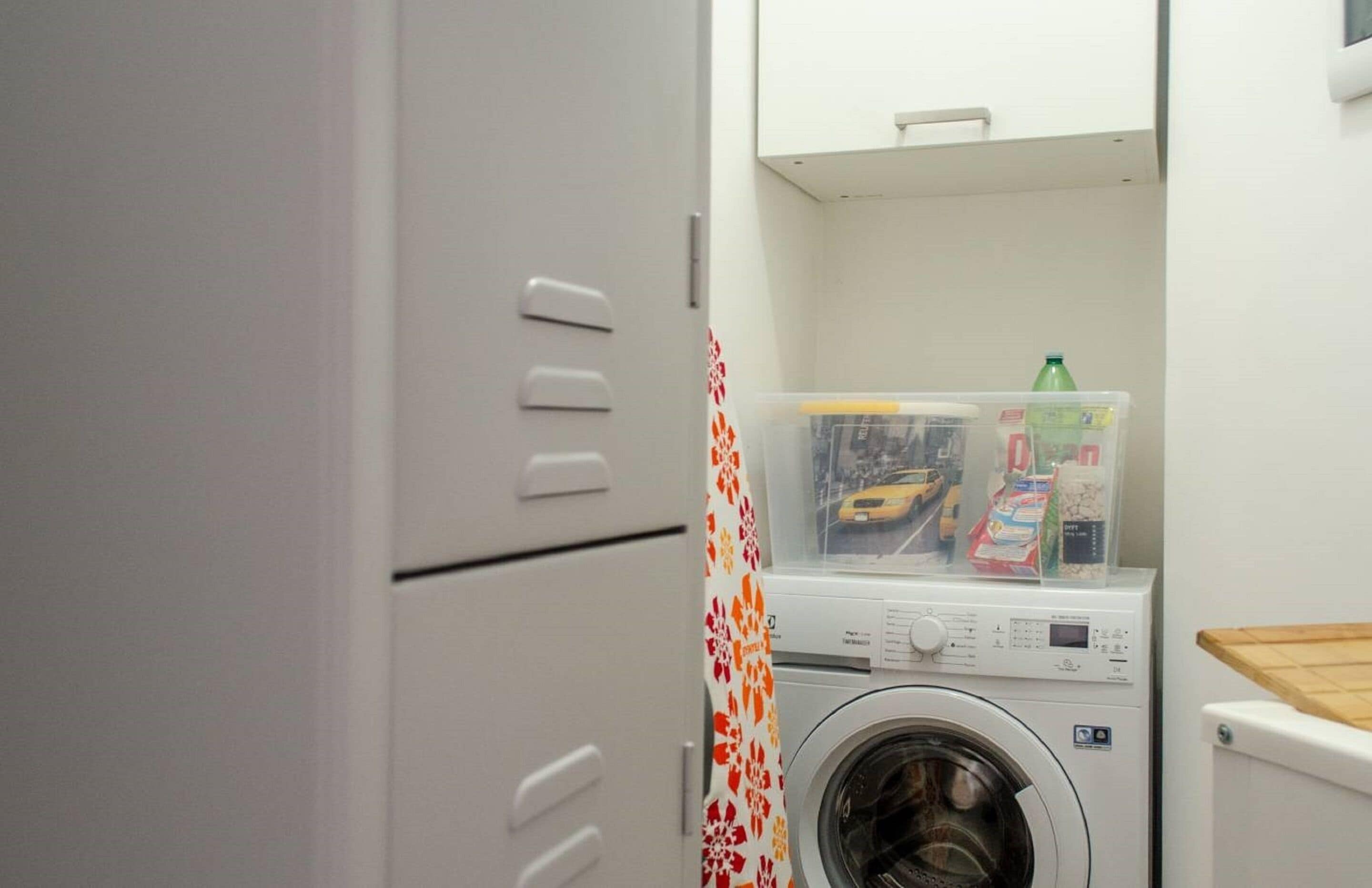 Un espace buanderie comprenant un lave-linge, un sèche-linge et un récipient en plastique contenant de la lessive.