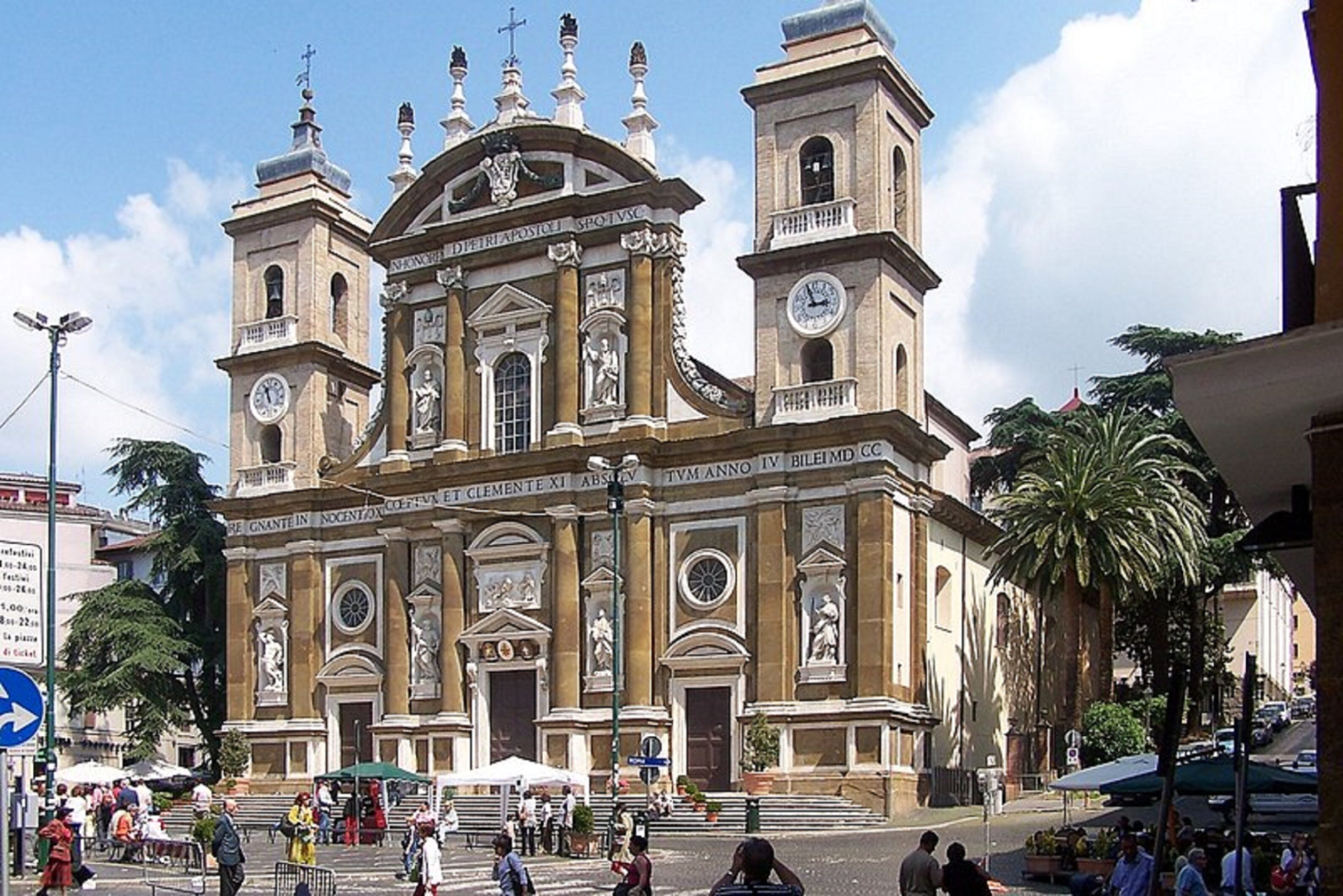 A historic church with a central dome and two bell towers, surrounded by a bustling square with pedestrians and outdoor seating.