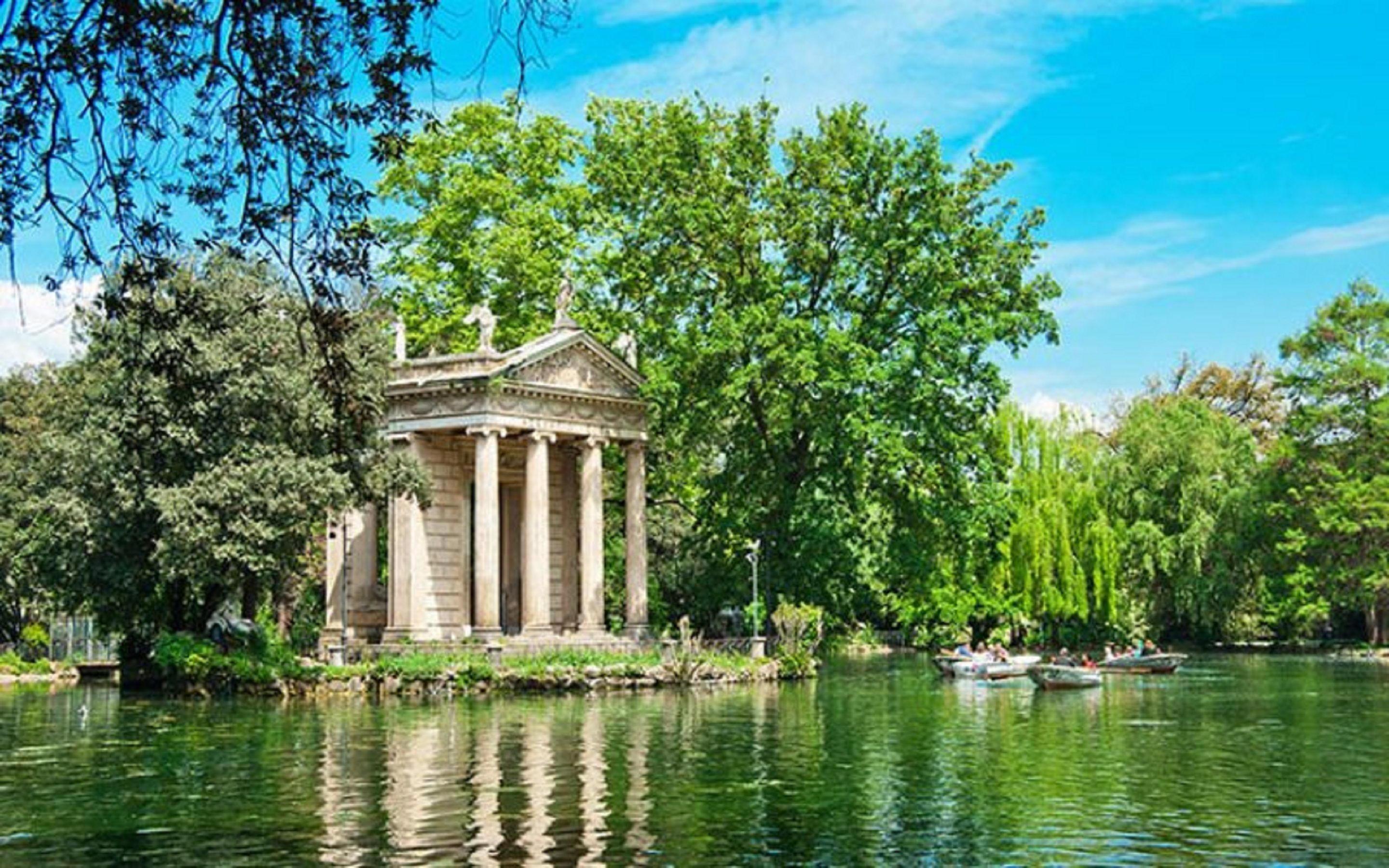A classical-style pavilion with columns, surrounded by lush greenery and a calm lake.