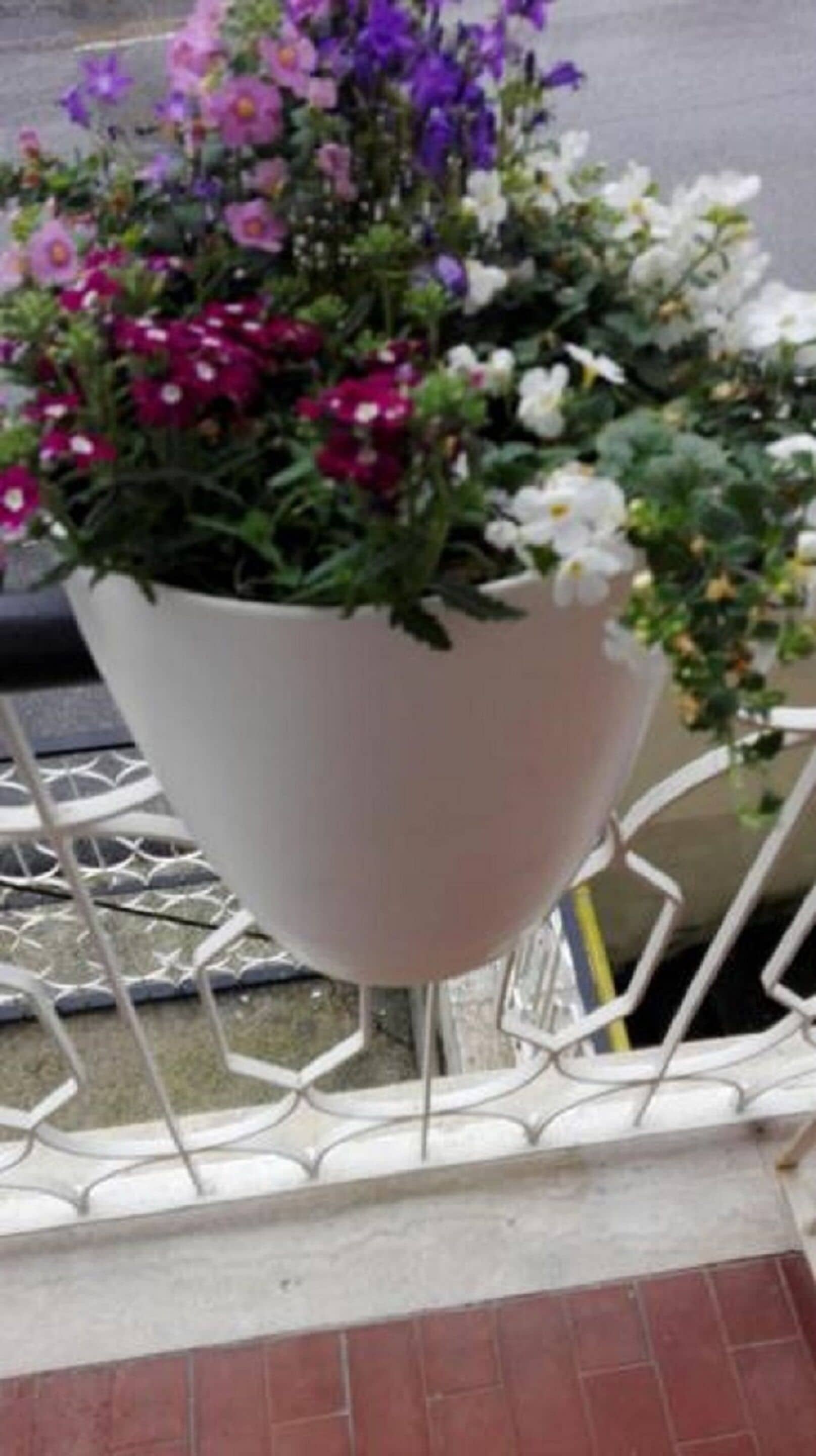 A white flower pot on a metal railing.