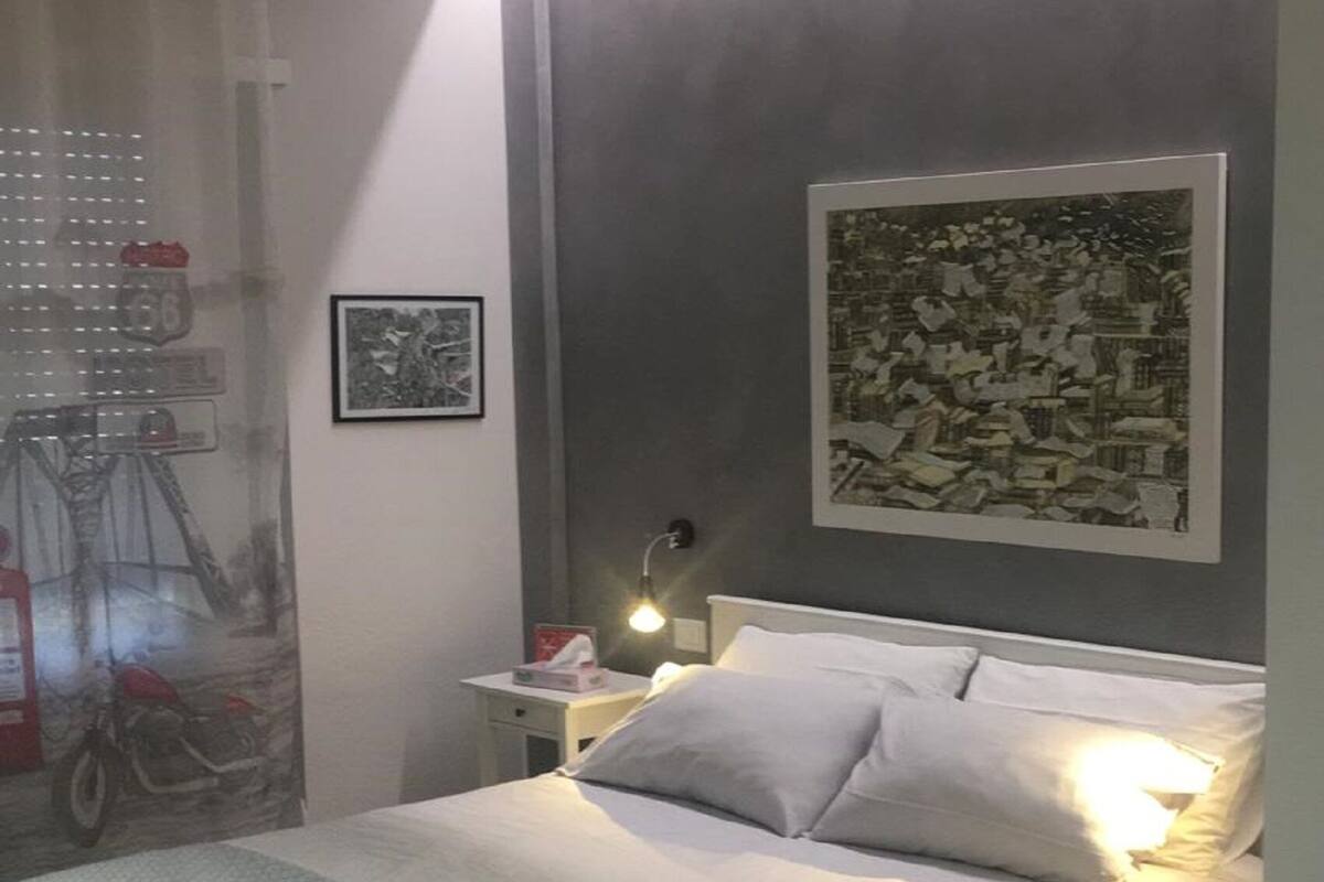 A neatly made bed with a patterned blanket, a bedside table with a lamp, and a framed picture on the wall.