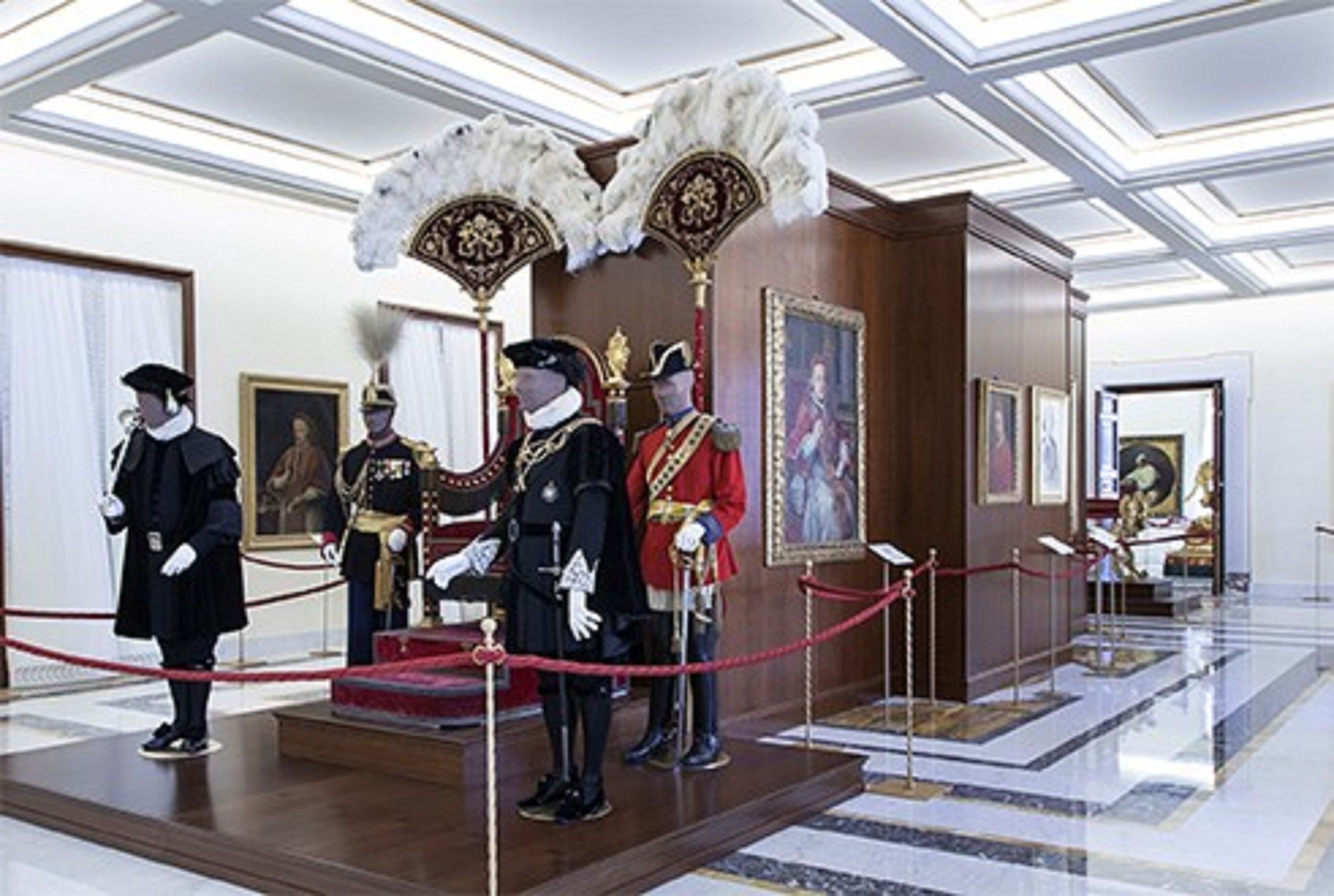 Una sala formal con alfombra roja, un atril y cuatro personas con atuendo ceremonial.