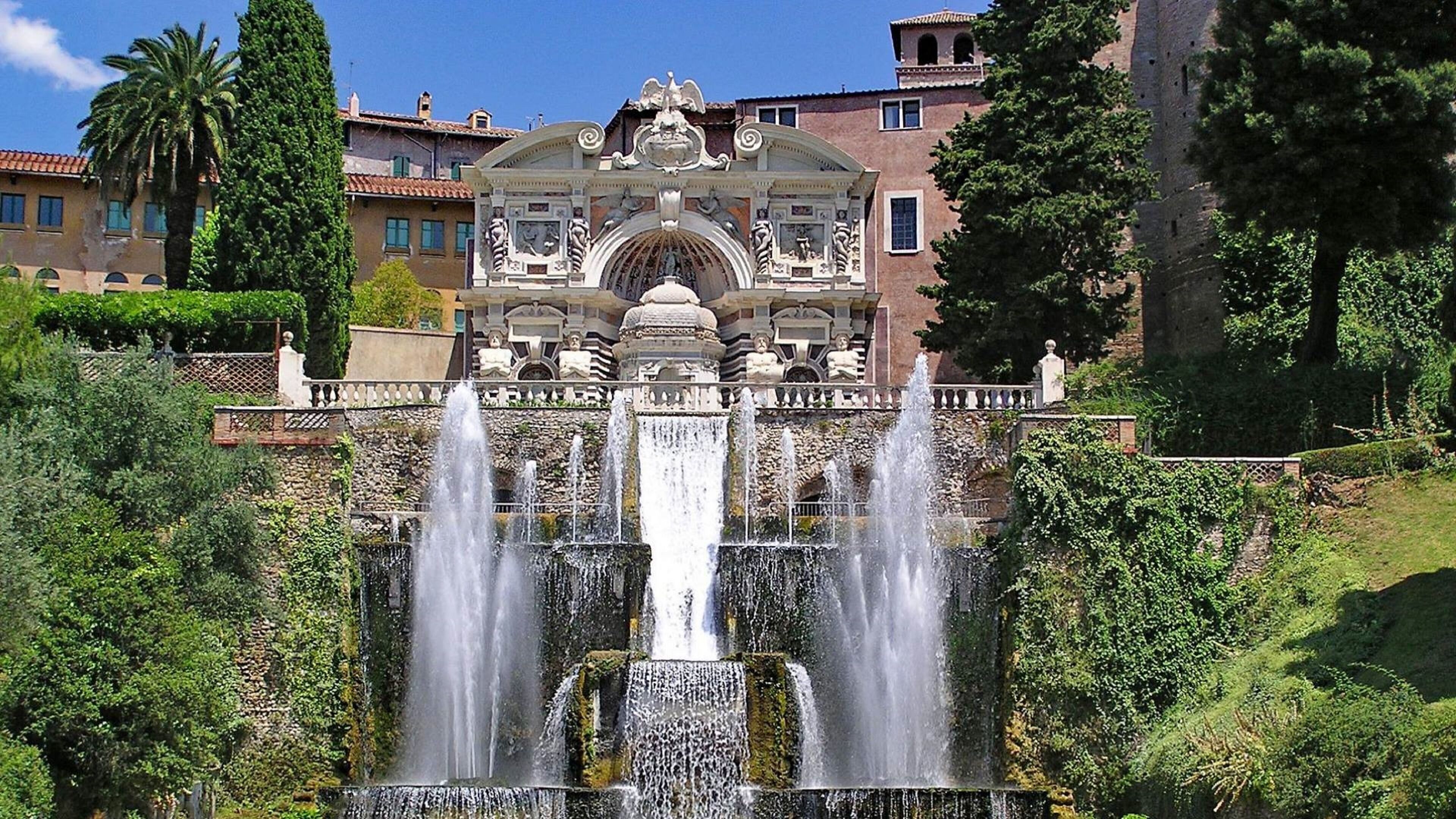 Une magnifique fontaine dotée de nombreux jets d’eau, entourée d’une végétation luxuriante et d’une architecture classique.