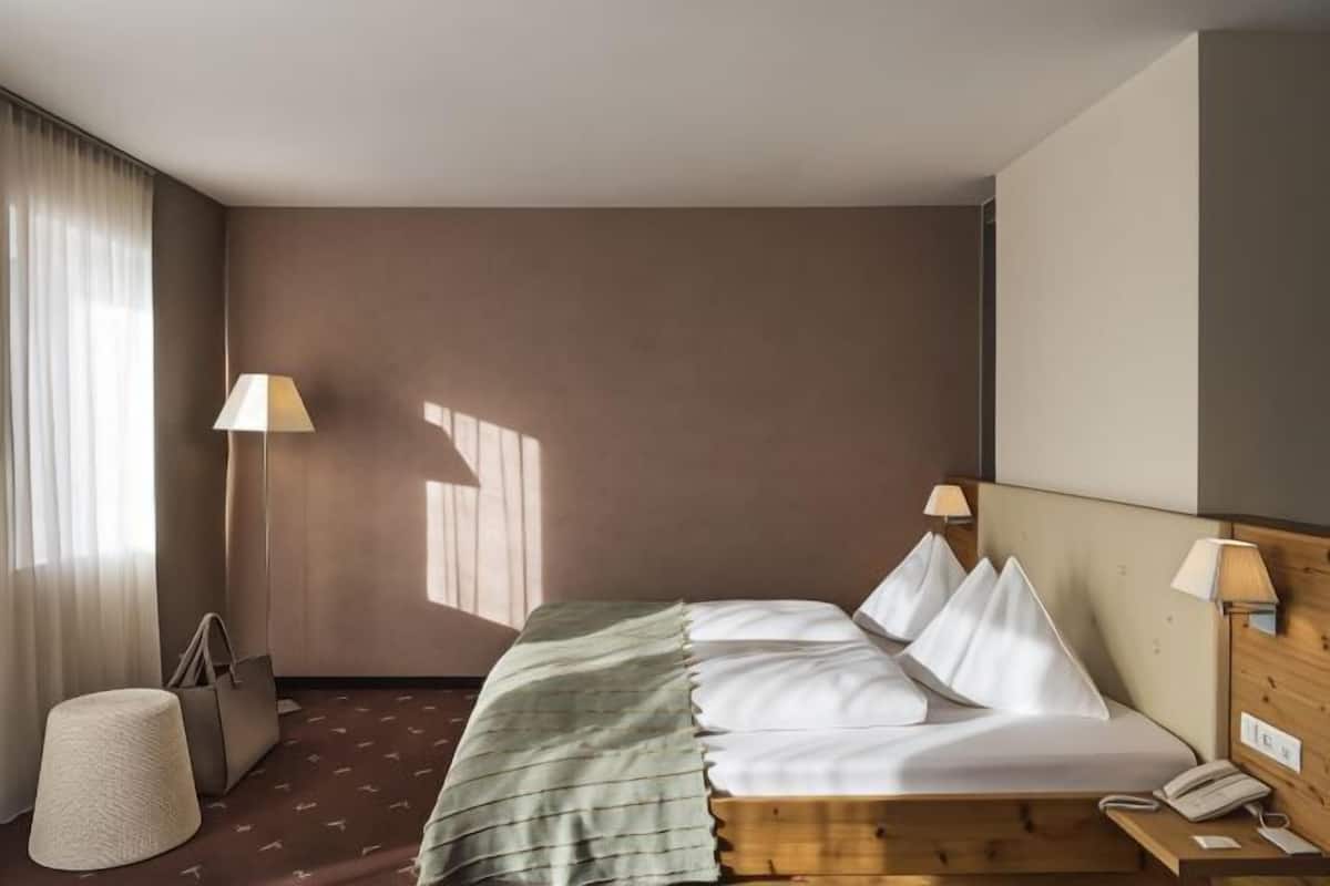 A hotel room with a bed, bedside lamps, a telephone, a handbag, and a lamp on a table.