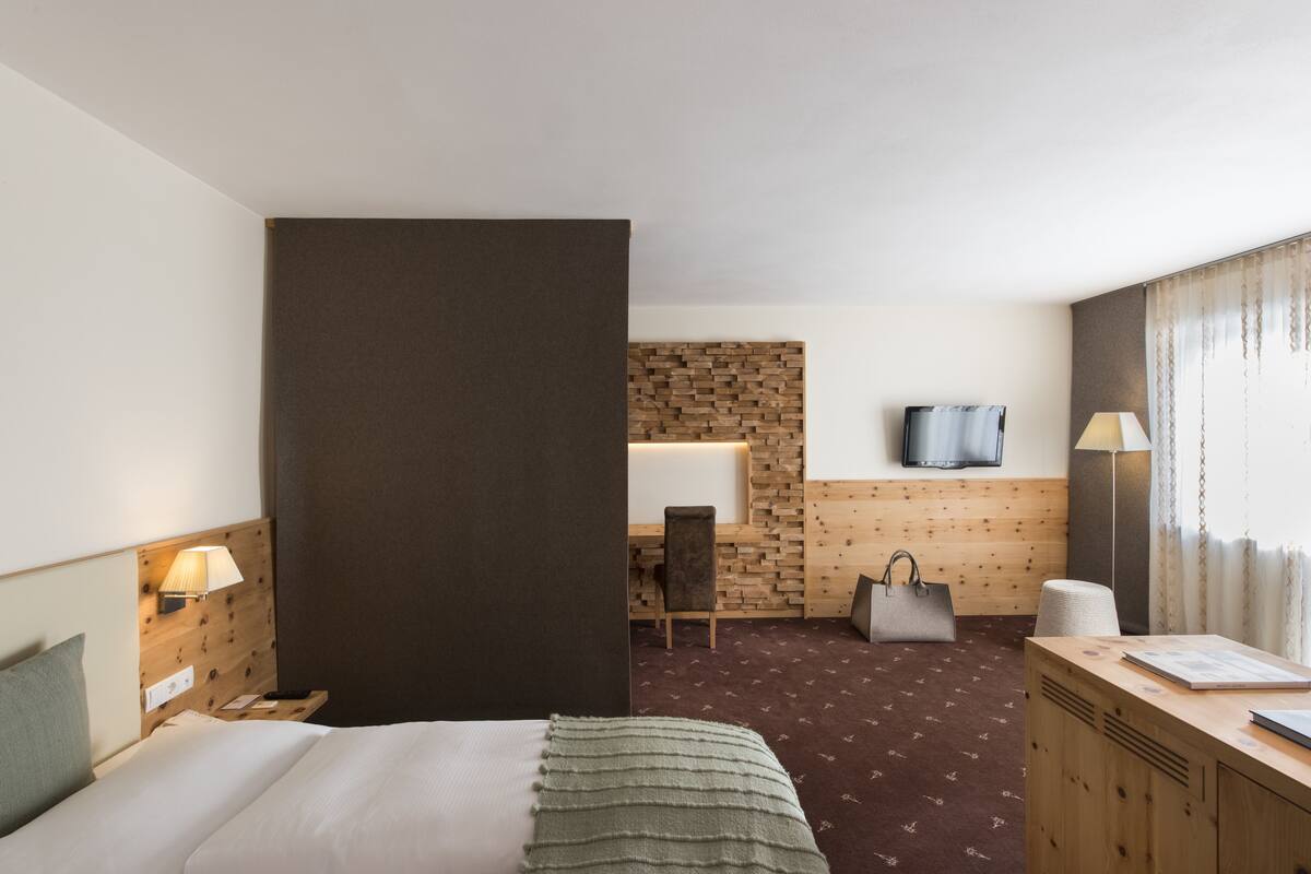 A hotel room with a bed, a desk, a chair, a TV, and a lamp.