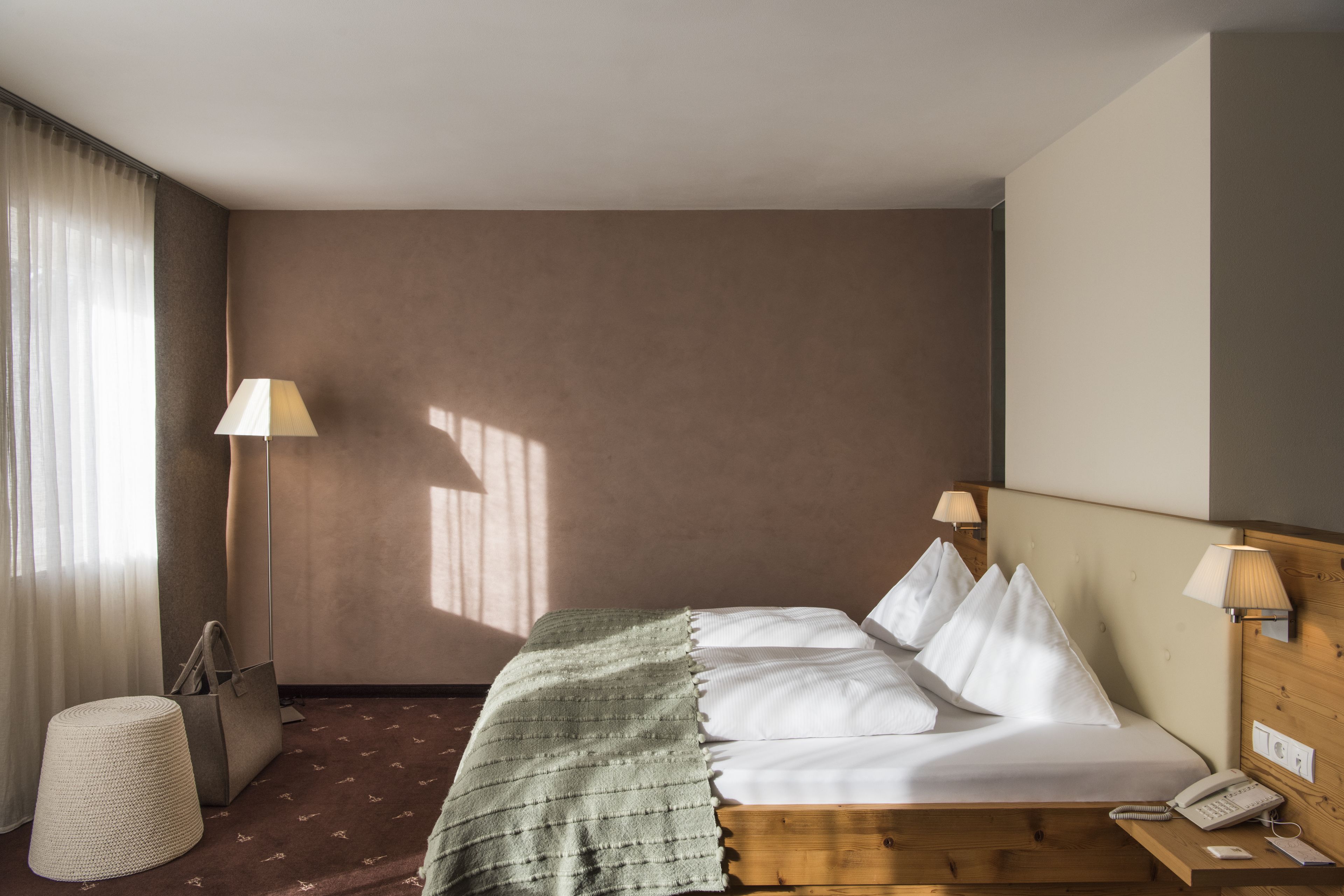 Una habitación de hotel con cama, lámparas de noche, un teléfono, un bolso y una lámpara sobre una mesita.