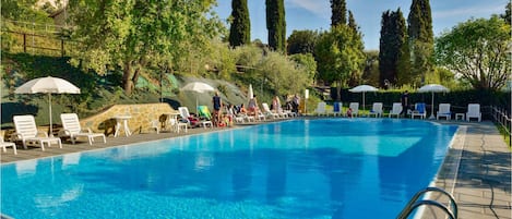 Una piscina al aire libre, sombrillas, sillones reclinables de piscina