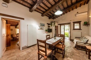Uma sala de jantar com uma mesa e cadeiras de madeira, uma televisão em um armário e vista para o exterior através de uma porta.