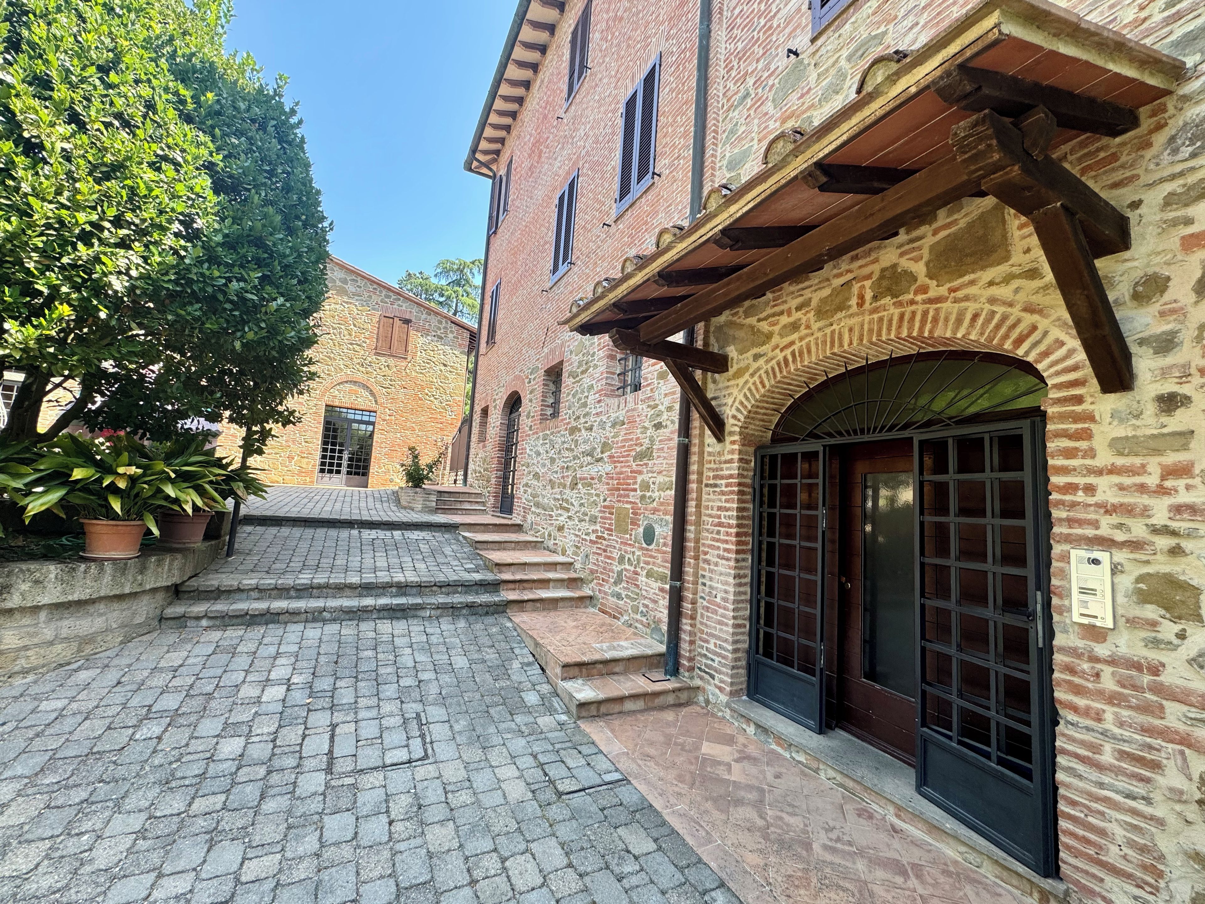 Un cortile con sentieri in pietra, edifici in pietra con portali ad arco e piante in vaso.