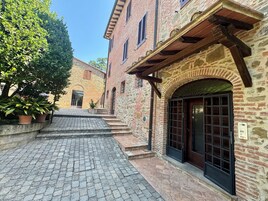 A courtyard with cobblestone paths, stone buildings with arched doorways, and potted plants.