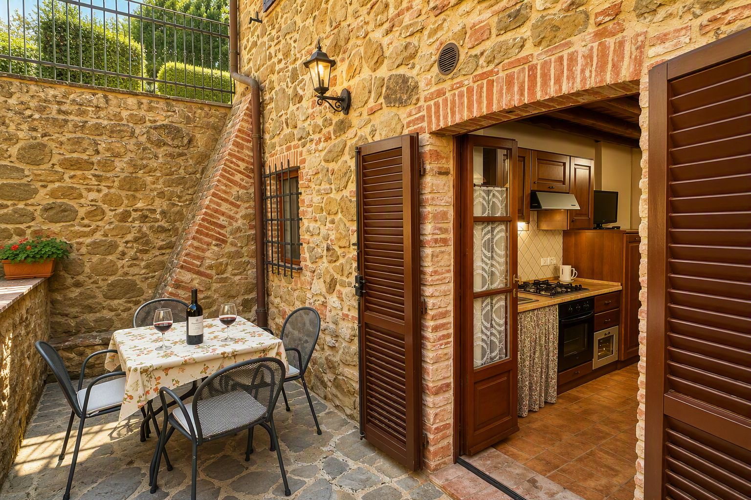 Un edificio in pietra con un tavolo e sedie in veranda, una cucina con mobili in legno e un piccolo giardino.