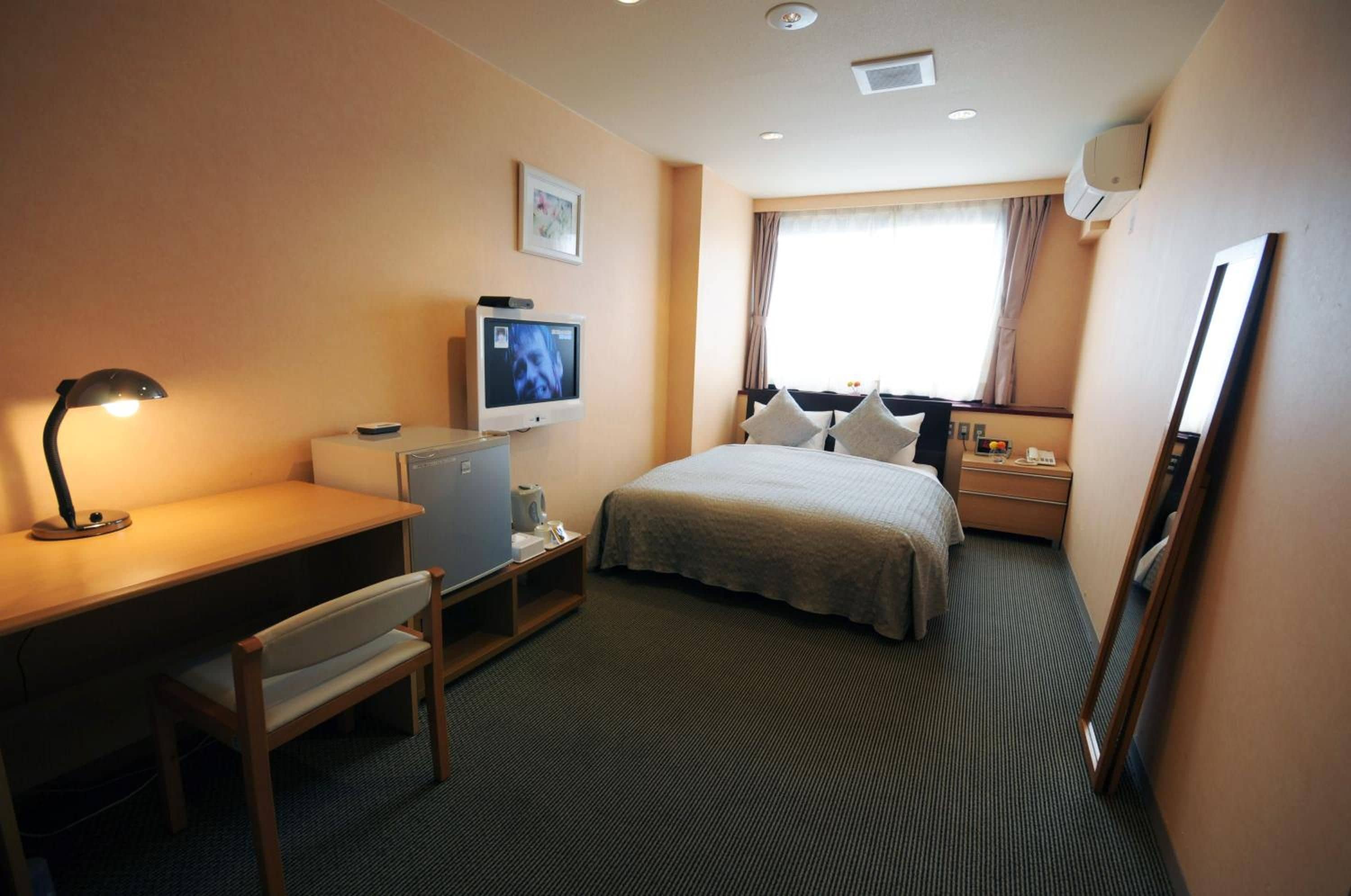 Una camera d'albergo con un letto, una scrivania, una sedia, televisione e una finestra con tende.