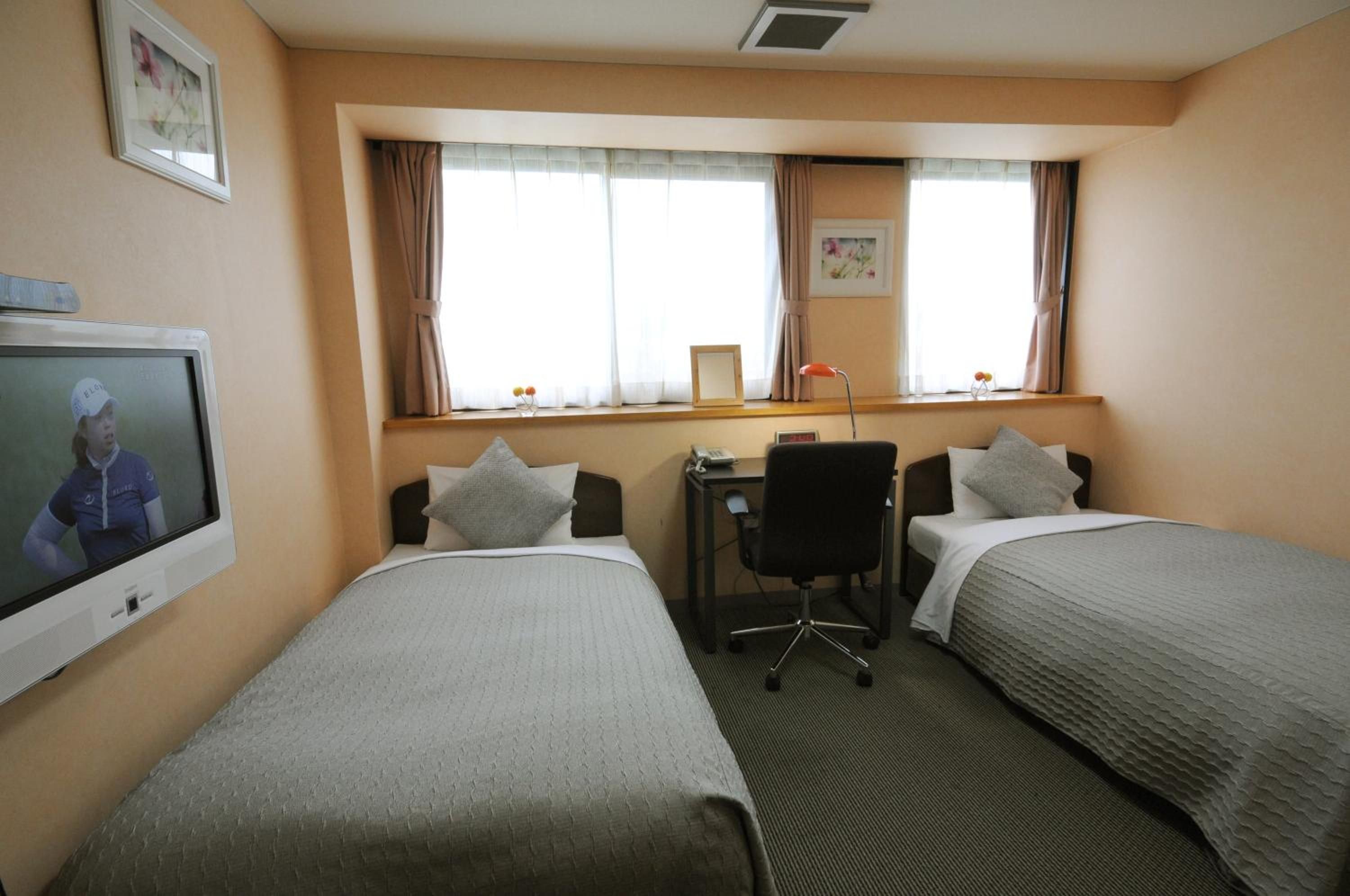 A hotel room with two beds, a desk, a chair, a television, and a window with curtains.