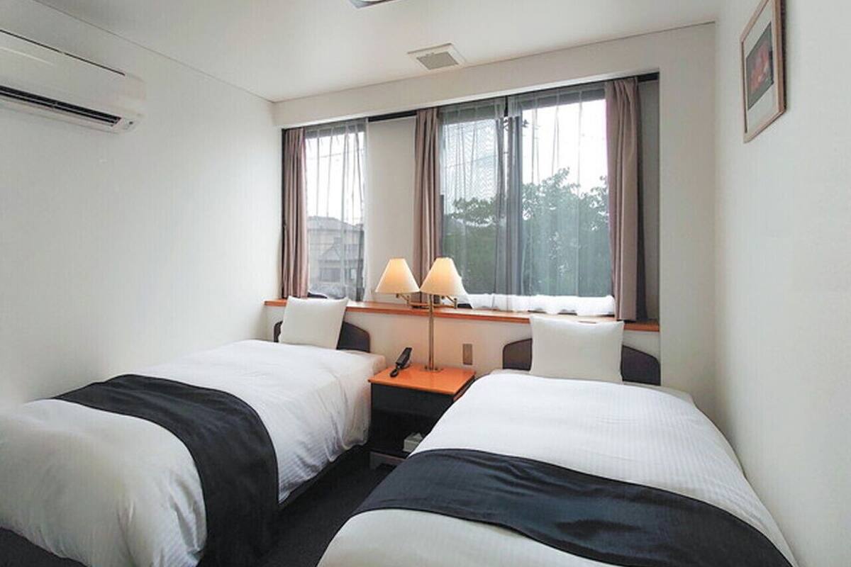 A hotel room with two beds, a desk with a lamp, a phone, and a window with curtains.