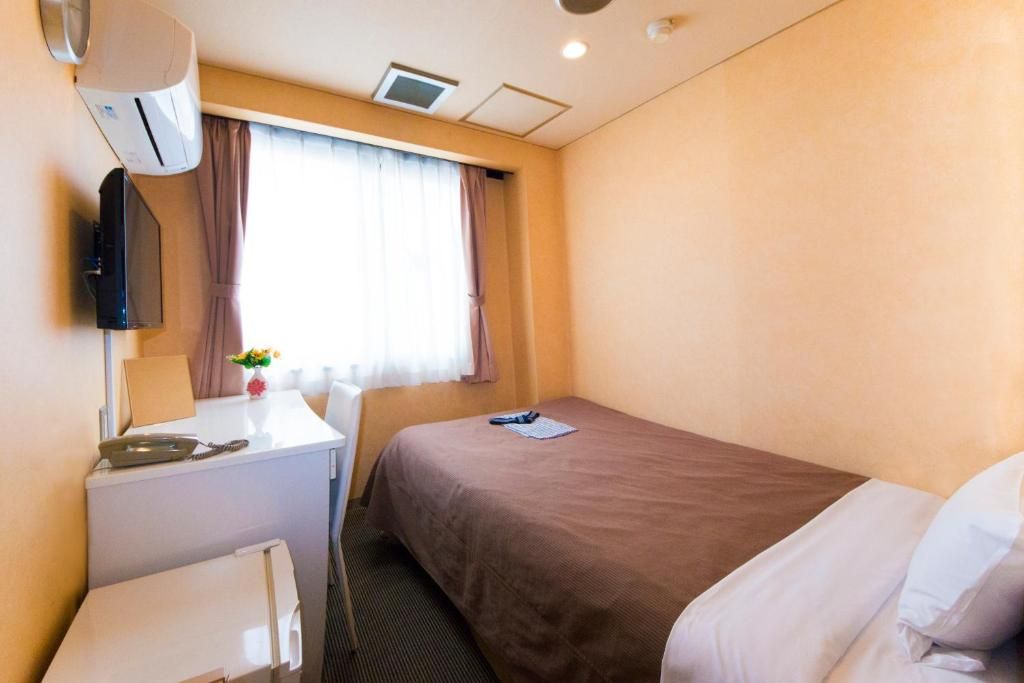 A hotel room with a bed, a desk, a chair, an air conditioning unit, and a window with curtains.