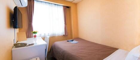 A hotel room with a bed, a desk, a chair, an air conditioning unit, and a window with curtains.