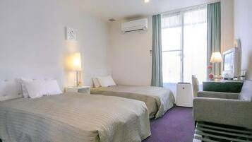 Una habitación de hotel con dos camas, un escritorio con una computadora, una silla y un ventanal con cortinas.