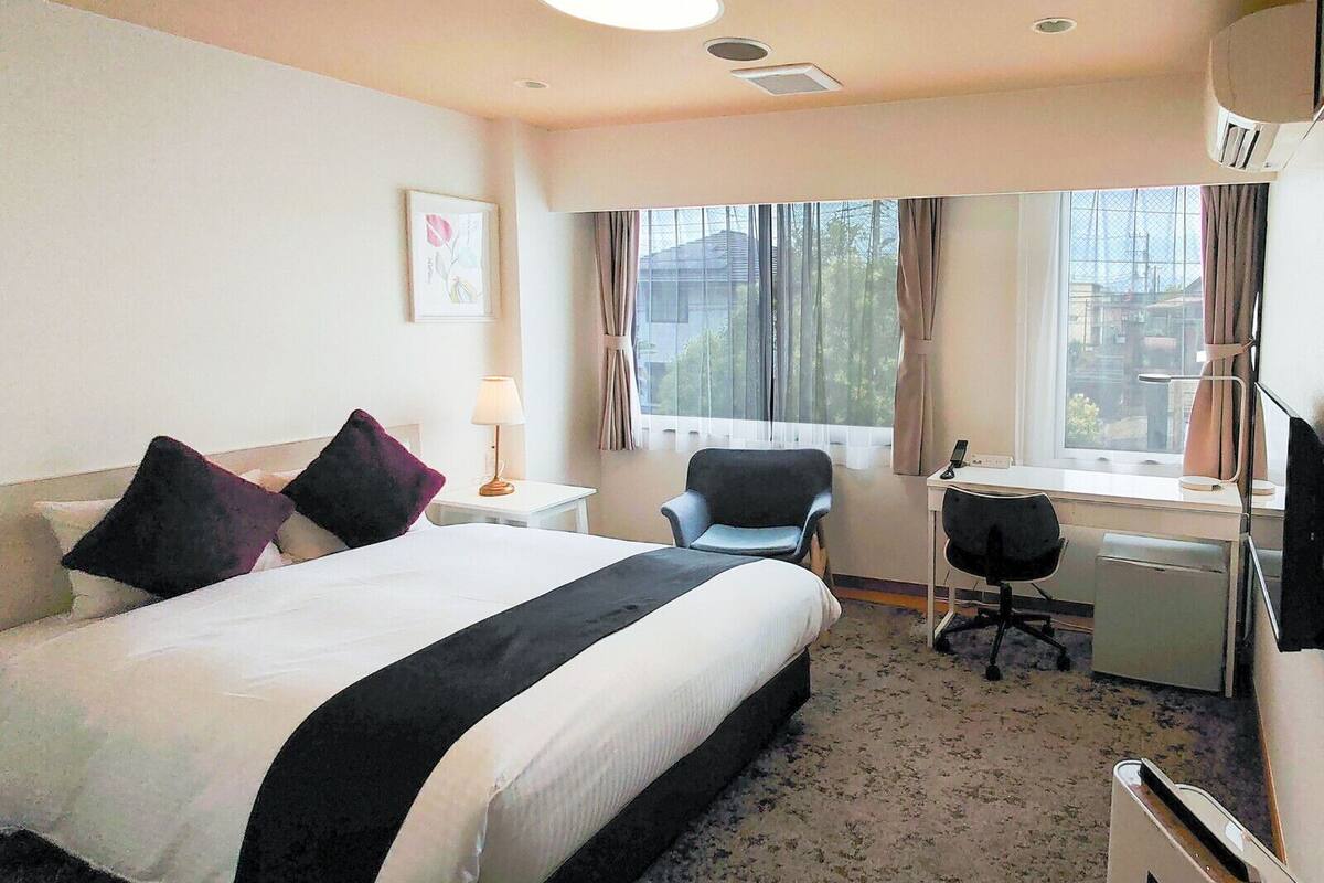 A hotel room with a bed, desk, chair, and a window with curtains.