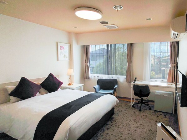 Una habitación de hotel con cama, escritorio, silla y ventana con cortinas.