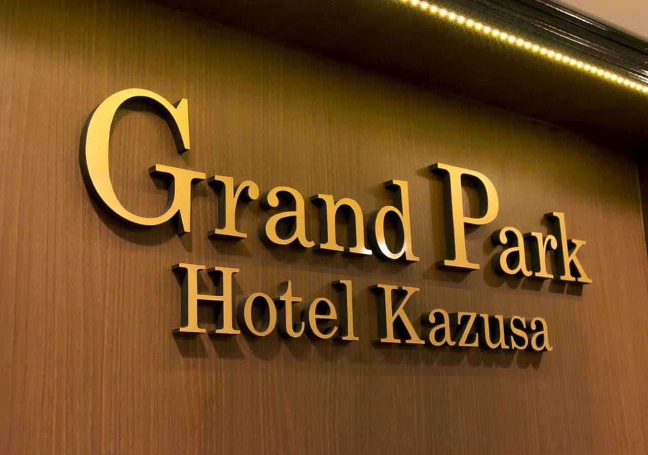 A sign for Grand Park Hotel Kazusa with a wooden background and illuminated lettering.