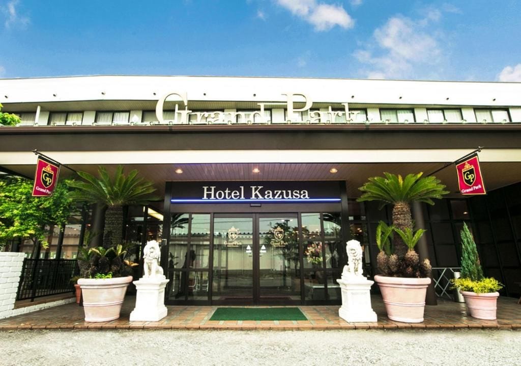 The entrance to Hotel Kazusa with a clear sign, potted plants, and a statue.