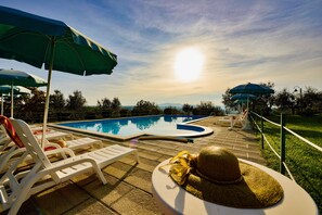 Zona de piscina amb gandules, ombrelles i un barret sobre una taula.