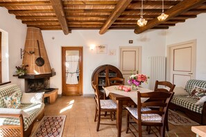 Una habitación acogedora con chimenea, vigas de madera en el techo, una mesa de comedor con sillas y un sofá a cuadros.