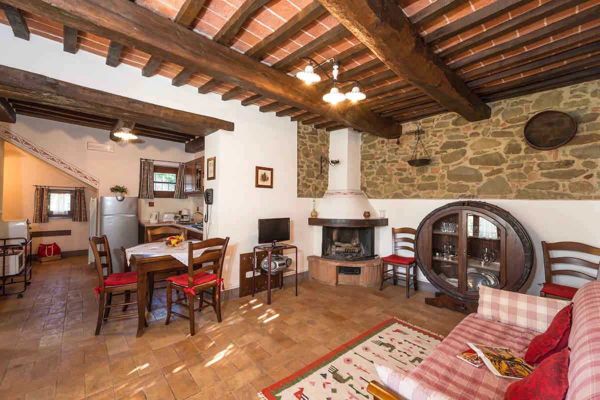 Un interior rústico con comedor, cocina y sala de estar, que presenta vigas de madera a la vista, paredes de piedra y una chimenea.