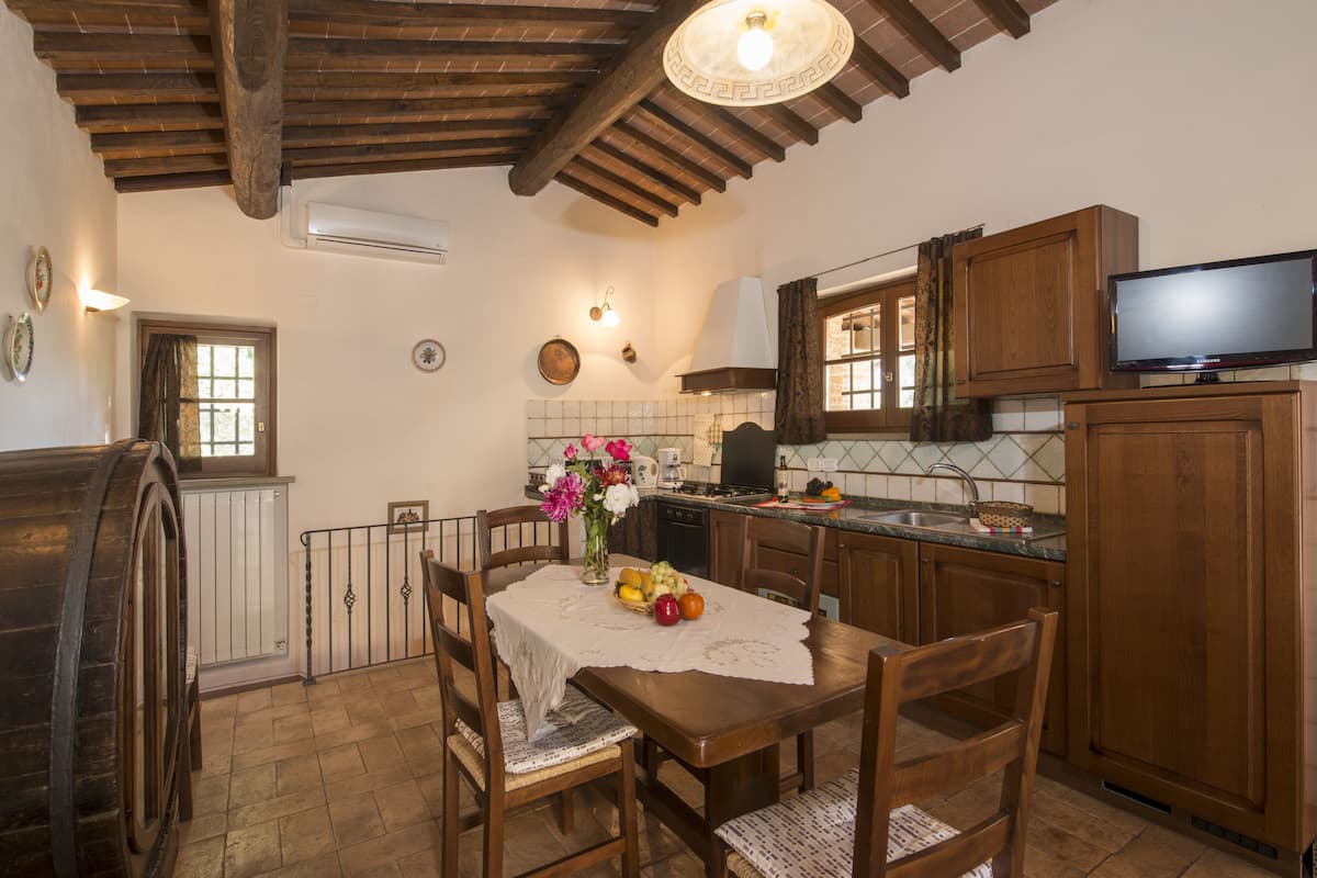 Una cocina rústica con armarios de madera, una mesa de comedor con sillas, un televisor y una ventana con cortinas.
