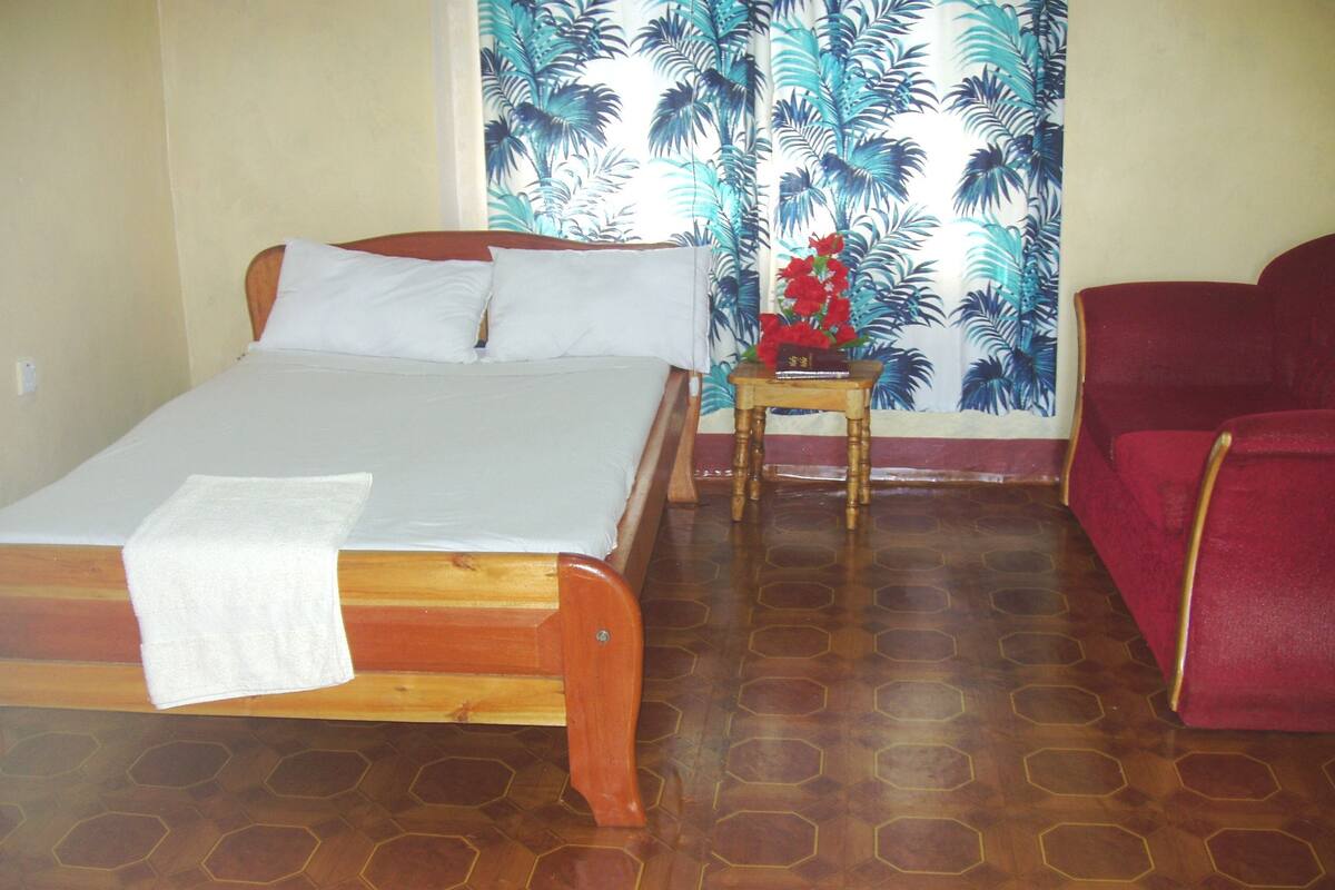 Quarto com cama de madeira, uma pequena mesa de madeira com um vaso de flores e uma cadeira vermelha.