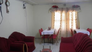 A dining area with red chairs and a table, a red sofa, and a small glass table in the center. - Imani Radio & TV Ministries (Kitale)