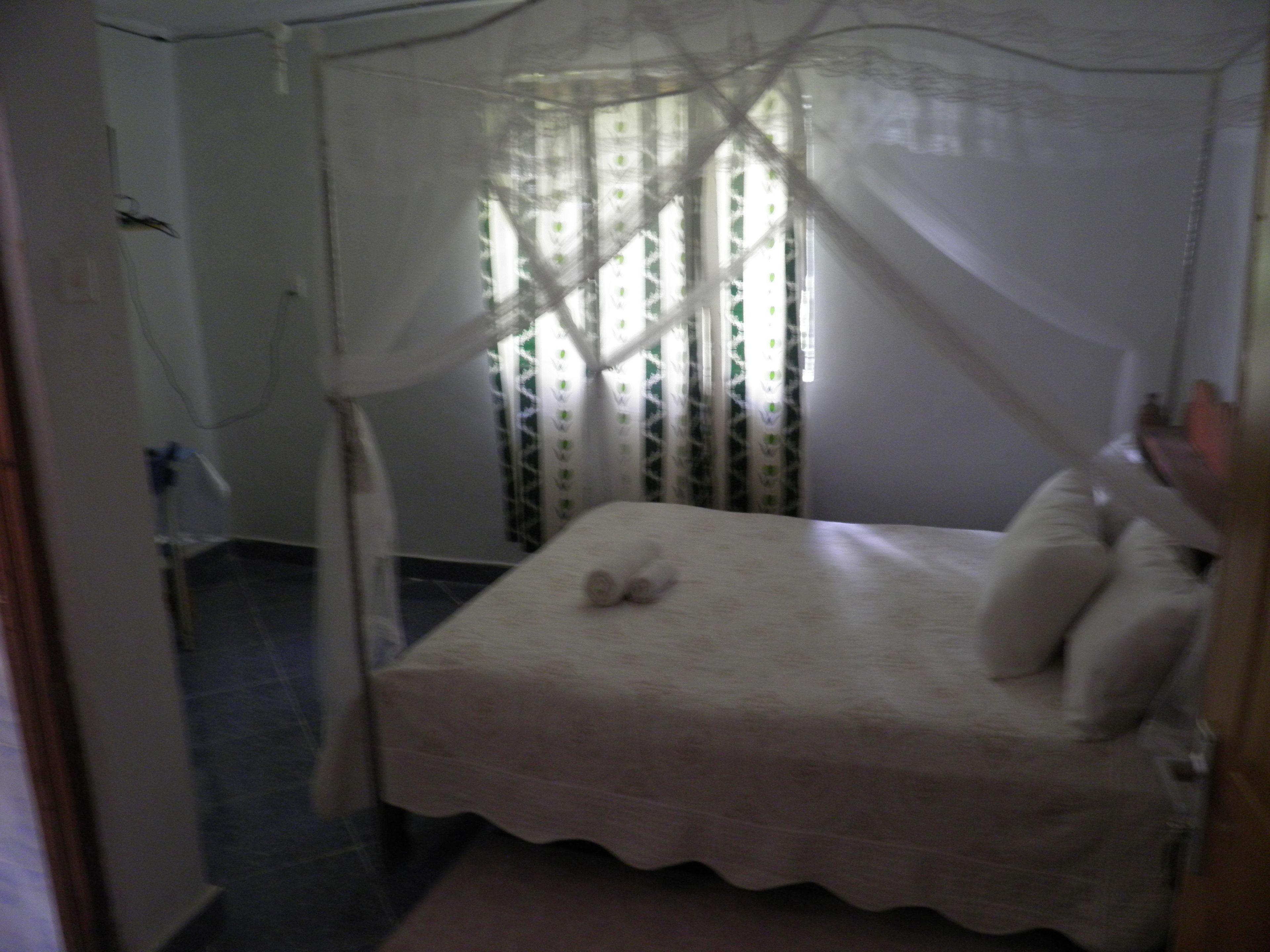 A bed with a canopy, a bedside table, and a window with patterned curtains.