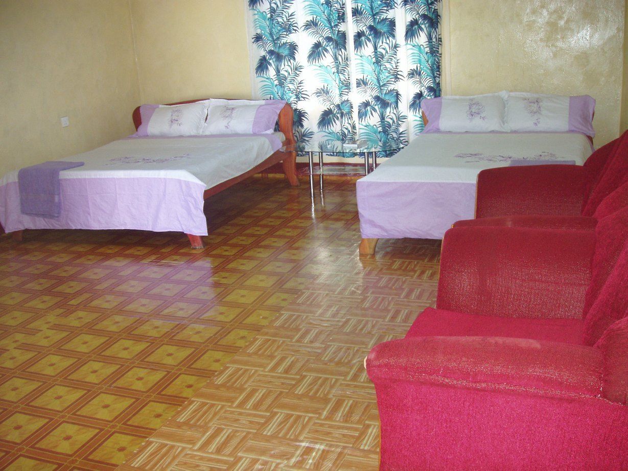 A room with two beds, a table, and a red sofa.