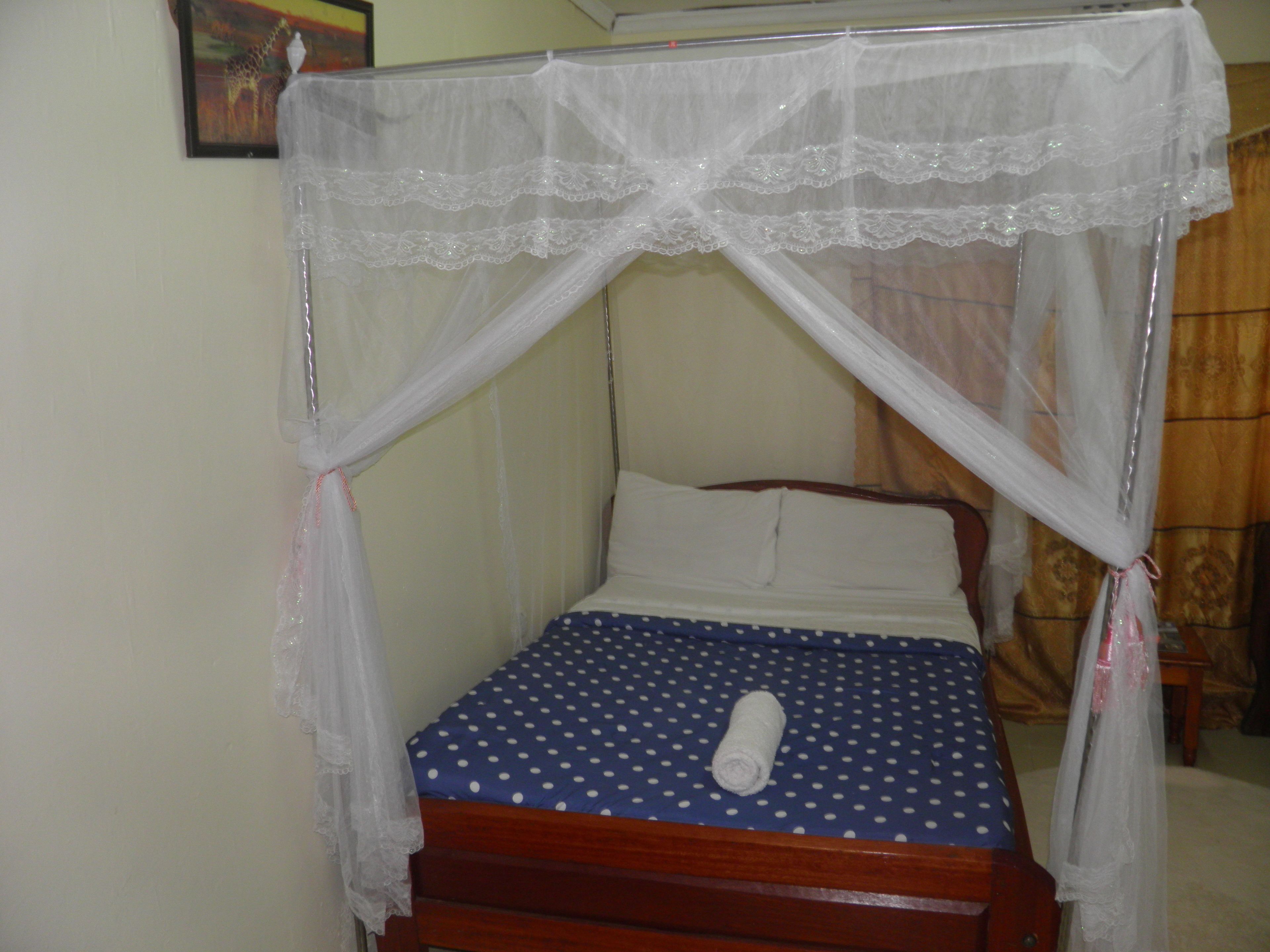 A single bed with a blue polka dot bedspread, white pillows, and a white canopy.